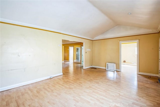 empty room featuring vaulted ceiling, ornamental molding, light wood-type flooring, and baseboards