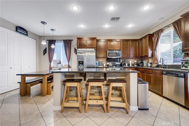 kitchen featuring light tile patterned floors, tasteful backsplash, visible vents, appliances with stainless steel finishes, and a kitchen breakfast bar