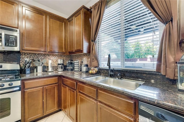 kitchen featuring light tile patterned floors, decorative backsplash, dark stone counters, stainless steel appliances, and a sink