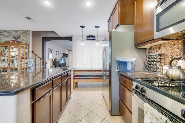 kitchen featuring light tile patterned flooring, stainless steel appliances, decorative backsplash, brown cabinets, and decorative light fixtures