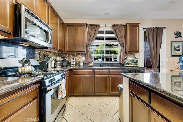 kitchen featuring light tile patterned floors, appliances with stainless steel finishes, backsplash, dark stone countertops, and a sink