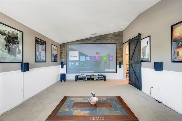 carpeted home theater room with lofted ceiling, a barn door, a wainscoted wall, and visible vents