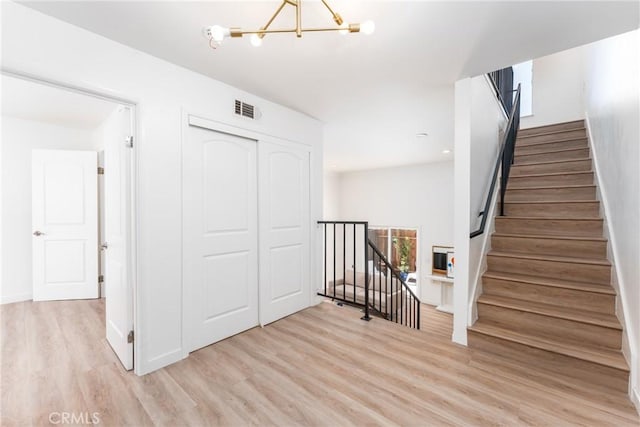 stairway featuring baseboards, wood finished floors, visible vents, and an inviting chandelier