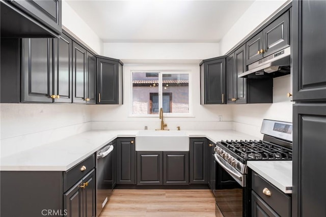 kitchen featuring light wood finished floors, appliances with stainless steel finishes, light countertops, under cabinet range hood, and a sink