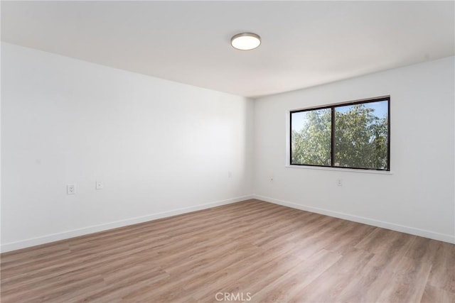 spare room featuring baseboards and light wood finished floors