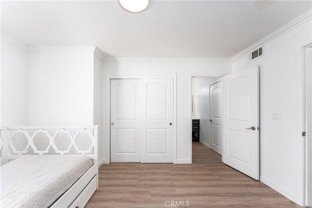 unfurnished bedroom with visible vents, baseboards, light wood-style floors, ornamental molding, and a closet