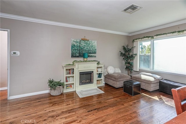 living area with ornamental molding, a glass covered fireplace, wood finished floors, and visible vents