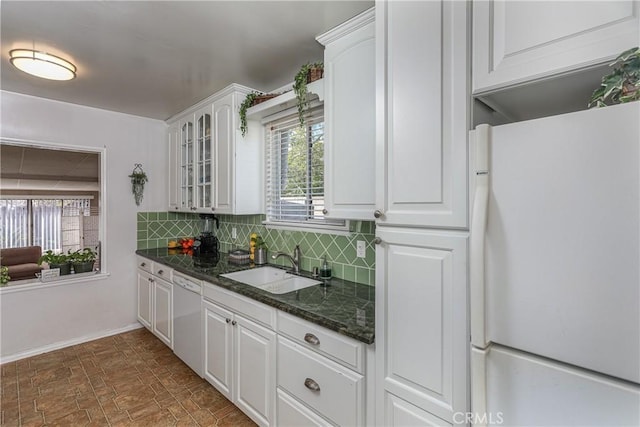 kitchen with decorative backsplash, glass insert cabinets, white cabinets, a sink, and white appliances