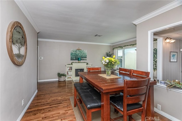 dining space featuring wood finished floors, visible vents, baseboards, a glass covered fireplace, and crown molding