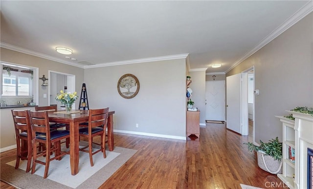 dining room featuring baseboards, a fireplace, wood finished floors, and crown molding