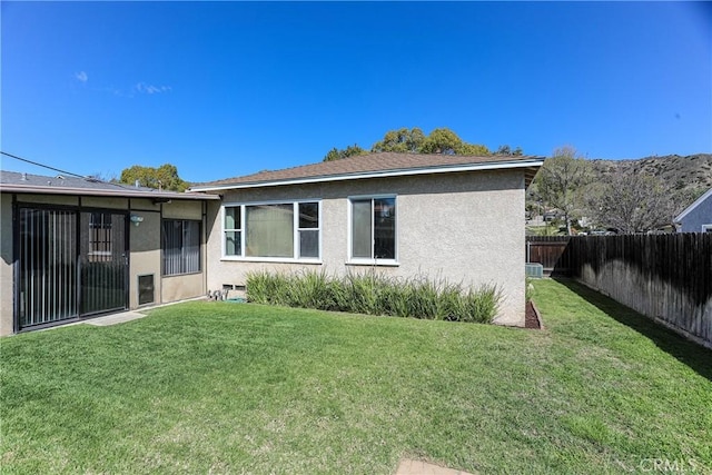 rear view of house with a fenced backyard, a lawn, and stucco siding