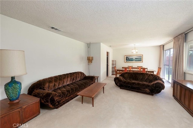 living area with visible vents, light colored carpet, a textured ceiling, and an inviting chandelier