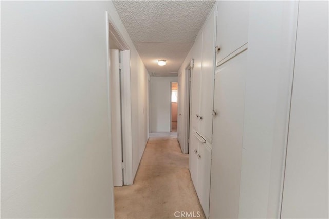 corridor with light colored carpet and a textured ceiling