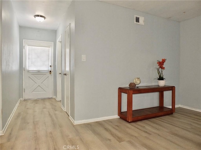 hall with baseboards, visible vents, and light wood finished floors