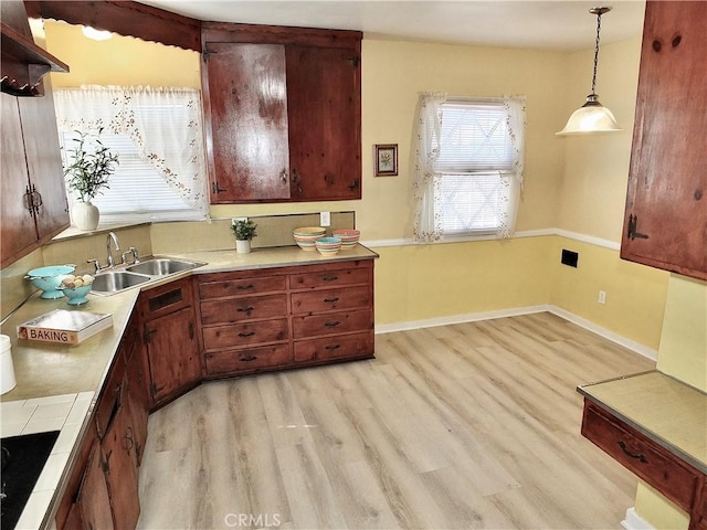 kitchen featuring light wood-style floors, pendant lighting, a sink, and baseboards