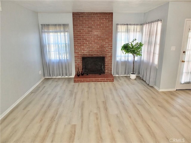 unfurnished living room featuring a brick fireplace, baseboards, and wood finished floors