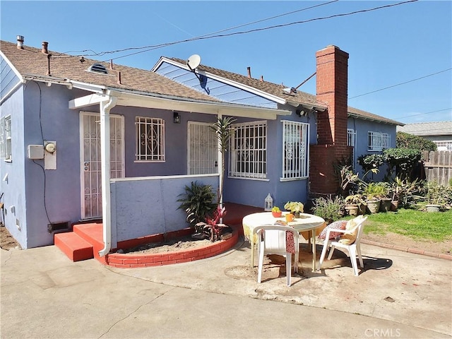 rear view of house with fence, roof with shingles, stucco siding, a chimney, and a patio area