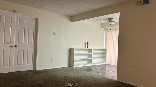 spare room featuring a textured ceiling, carpet flooring, visible vents, baseboards, and a ceiling fan