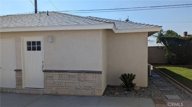 view of property exterior featuring central air condition unit, fence, stone siding, roof with shingles, and stucco siding