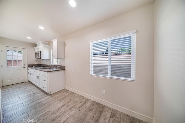 kitchen featuring light wood-style flooring, a sink, white cabinets, stainless steel microwave, and dark countertops