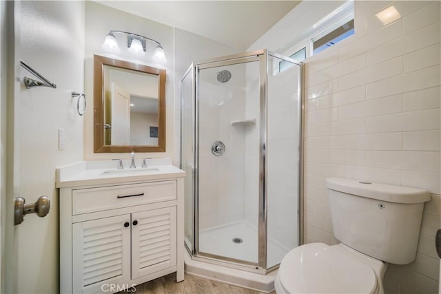 full bathroom with vanity, a shower stall, toilet, and tile walls