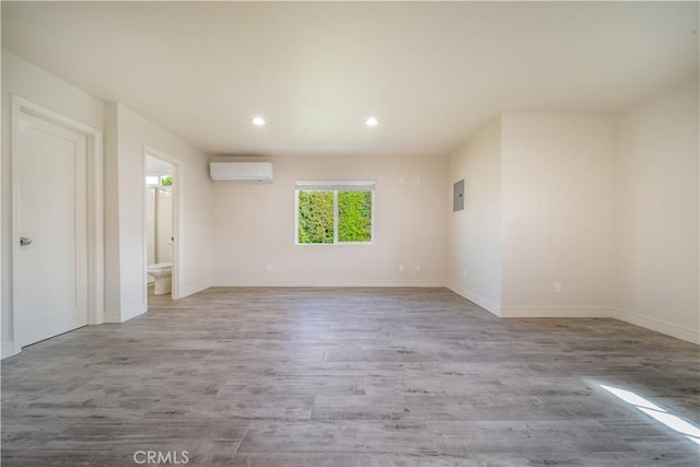 empty room featuring electric panel, baseboards, wood finished floors, a wall mounted AC, and recessed lighting