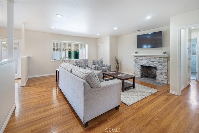 living area featuring recessed lighting, baseboards, a stone fireplace, and light wood finished floors