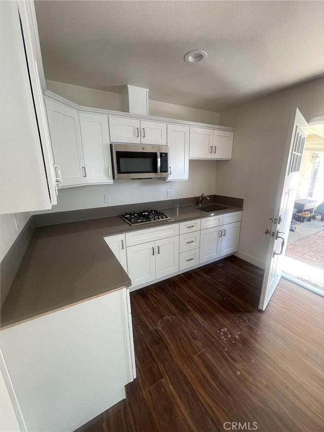 kitchen with white cabinets, dark wood finished floors, dark countertops, appliances with stainless steel finishes, and a sink