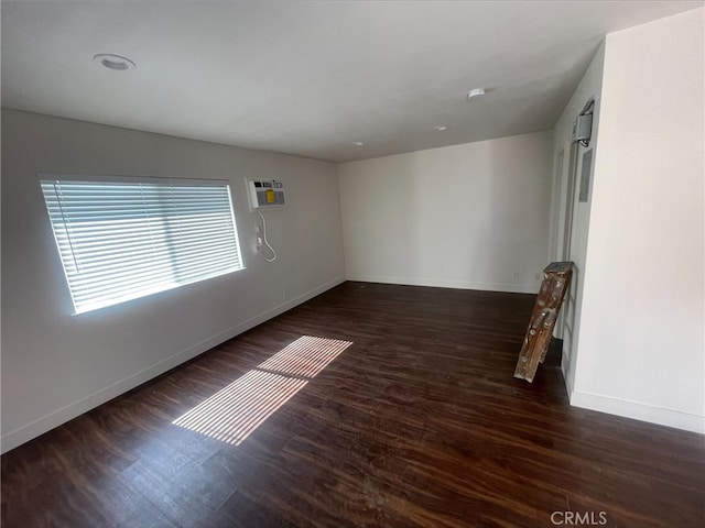 empty room featuring a wall mounted AC, wood finished floors, and baseboards