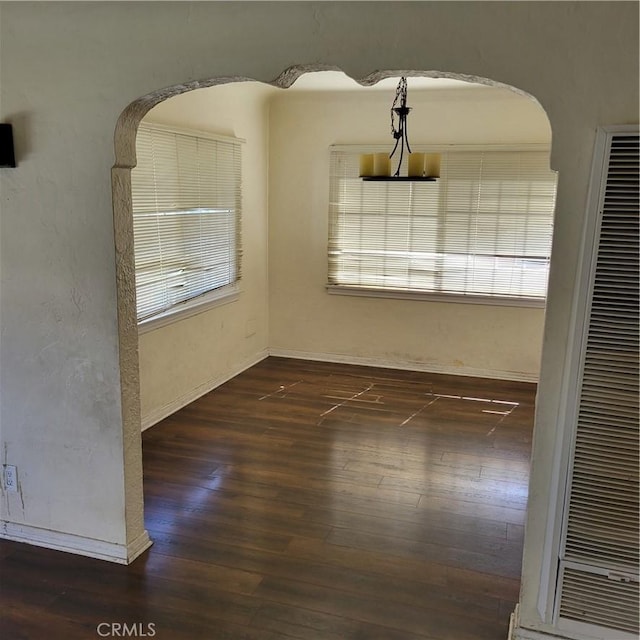 empty room featuring arched walkways, wood finished floors, and baseboards