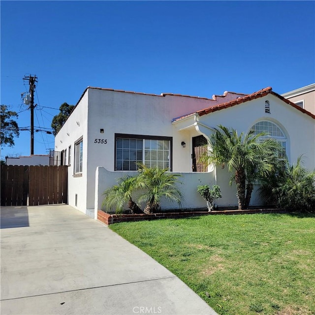 mediterranean / spanish-style home with fence, a front lawn, and stucco siding