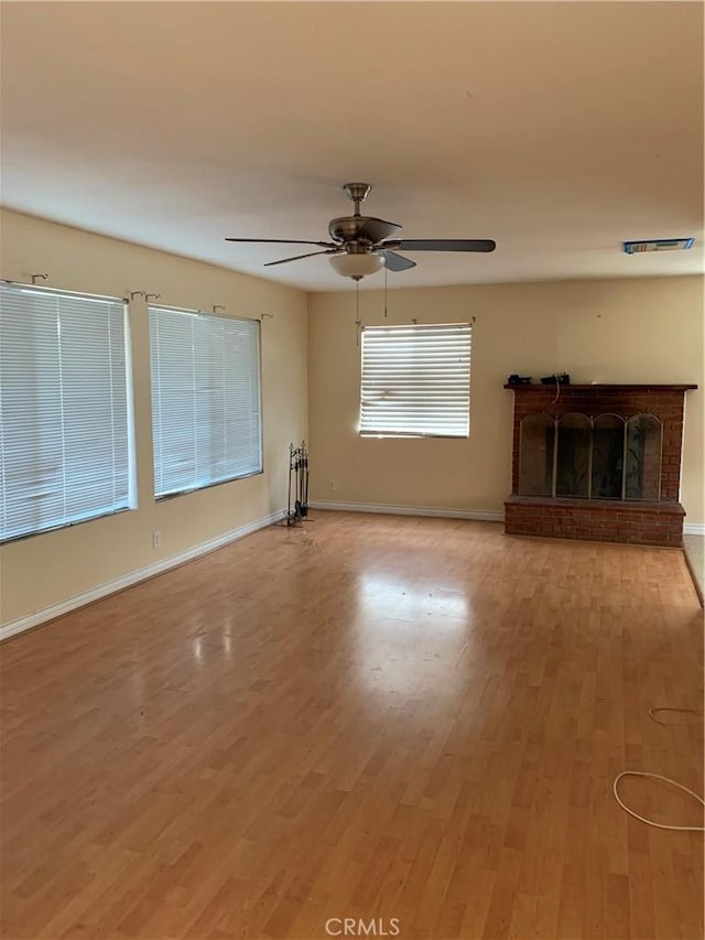 unfurnished living room featuring visible vents, a brick fireplace, ceiling fan, wood finished floors, and baseboards