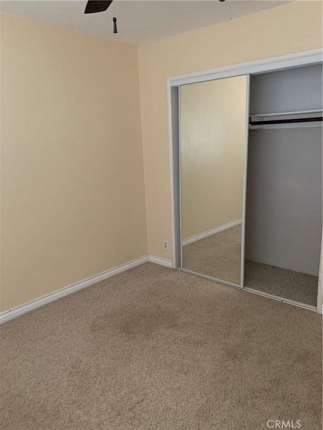 unfurnished bedroom with carpet floors, a closet, baseboards, and a ceiling fan