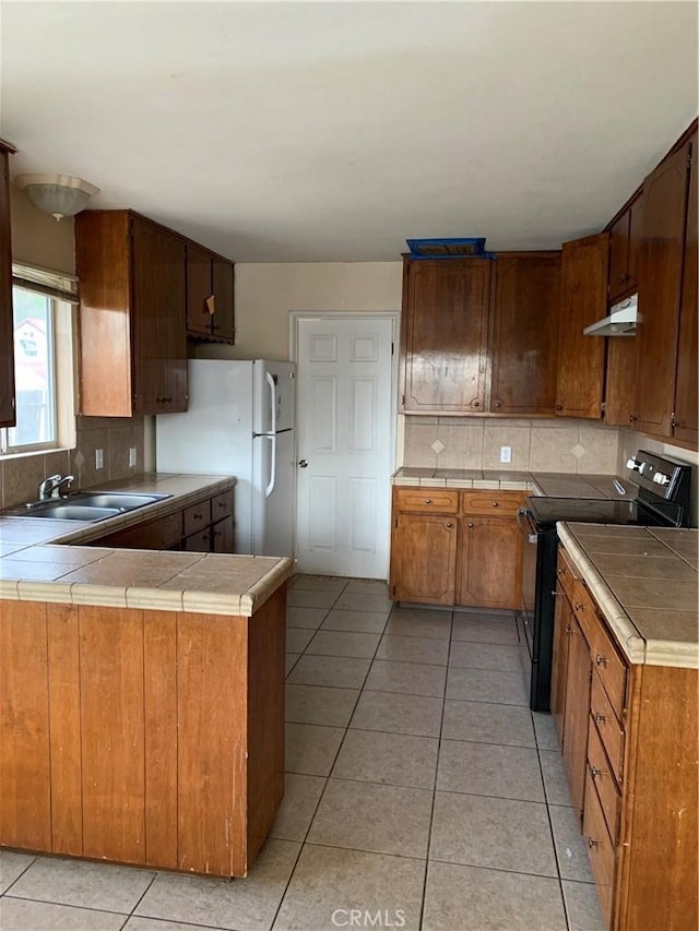 kitchen with tile counters, black range with electric stovetop, under cabinet range hood, and a sink