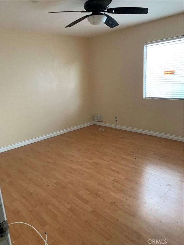 empty room featuring ceiling fan, light wood finished floors, and baseboards