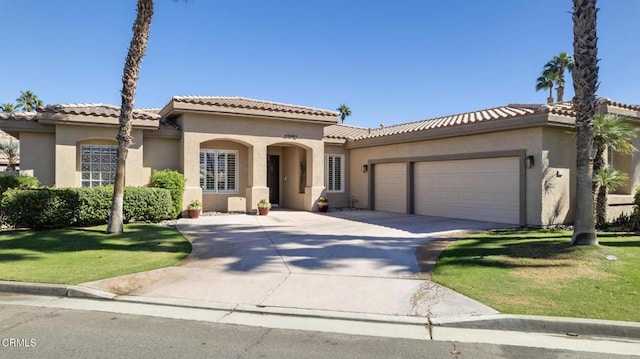 mediterranean / spanish home with a tile roof, stucco siding, a garage, driveway, and a front lawn