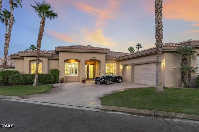 mediterranean / spanish house with a tile roof, stucco siding, a front yard, a garage, and driveway