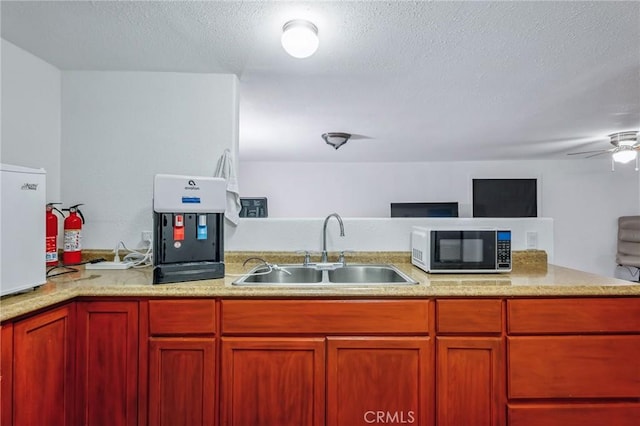 kitchen with ceiling fan, open floor plan, a peninsula, a textured ceiling, and a sink