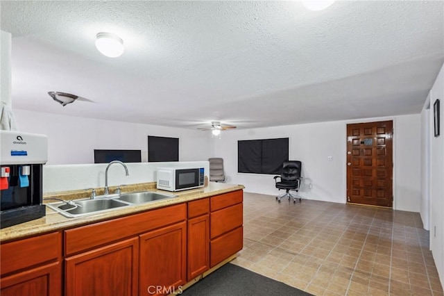 kitchen with white microwave, open floor plan, light countertops, a textured ceiling, and a sink