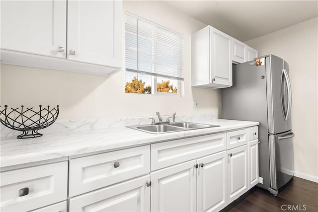 kitchen with white cabinets, dark wood-type flooring, freestanding refrigerator, light stone countertops, and a sink