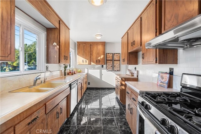 kitchen featuring appliances with stainless steel finishes, brown cabinets, light countertops, under cabinet range hood, and a sink