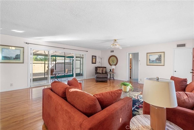 living area with visible vents, light wood-style flooring, ceiling fan, a textured ceiling, and baseboards