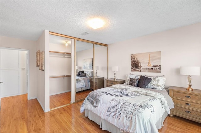 bedroom with a textured ceiling, light wood finished floors, a closet, and baseboards