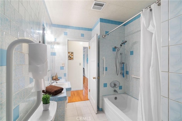 full bathroom with tile walls, shower / bath combination with curtain, visible vents, a sink, and tile patterned flooring