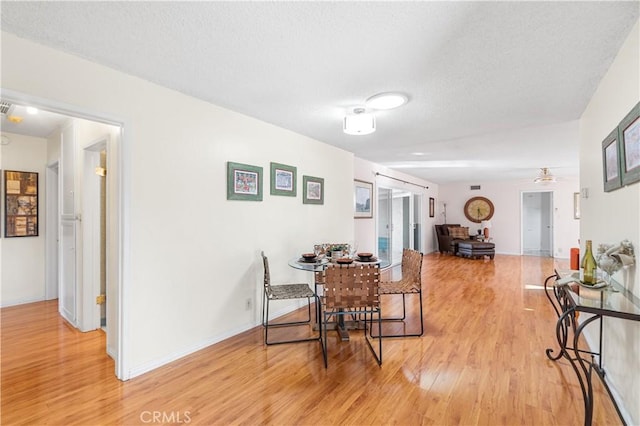 dining space with a textured ceiling, baseboards, light wood-style flooring, and a ceiling fan