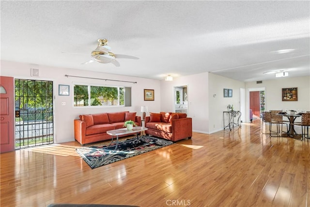 living area featuring light wood-style floors, visible vents, ceiling fan, and a textured ceiling