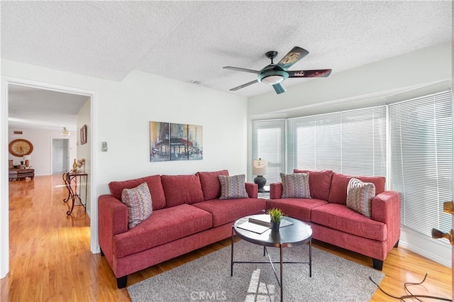 living area featuring light wood-style floors, visible vents, ceiling fan, and a textured ceiling