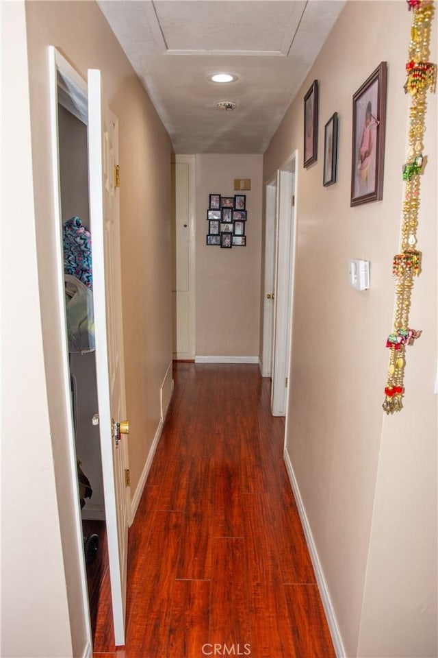 hall featuring dark wood-style floors, attic access, visible vents, and baseboards