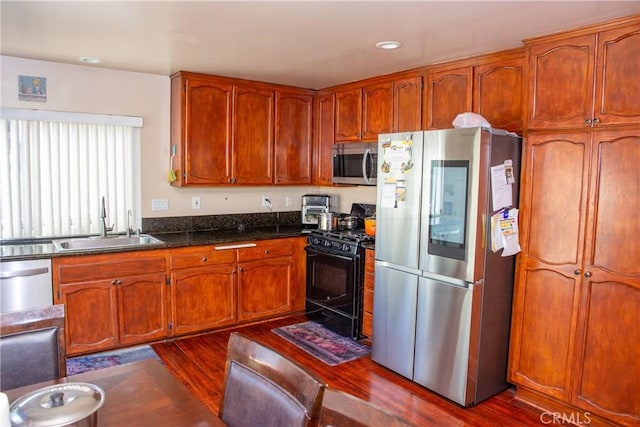 kitchen with appliances with stainless steel finishes, brown cabinetry, a sink, and dark wood finished floors