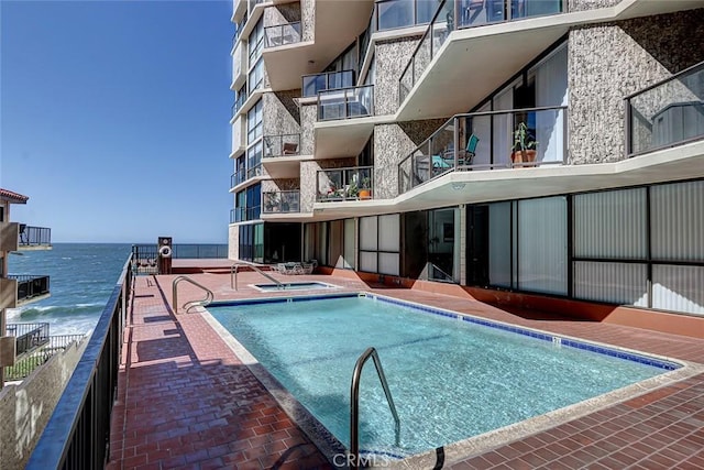 pool featuring a community hot tub, a water view, and a patio